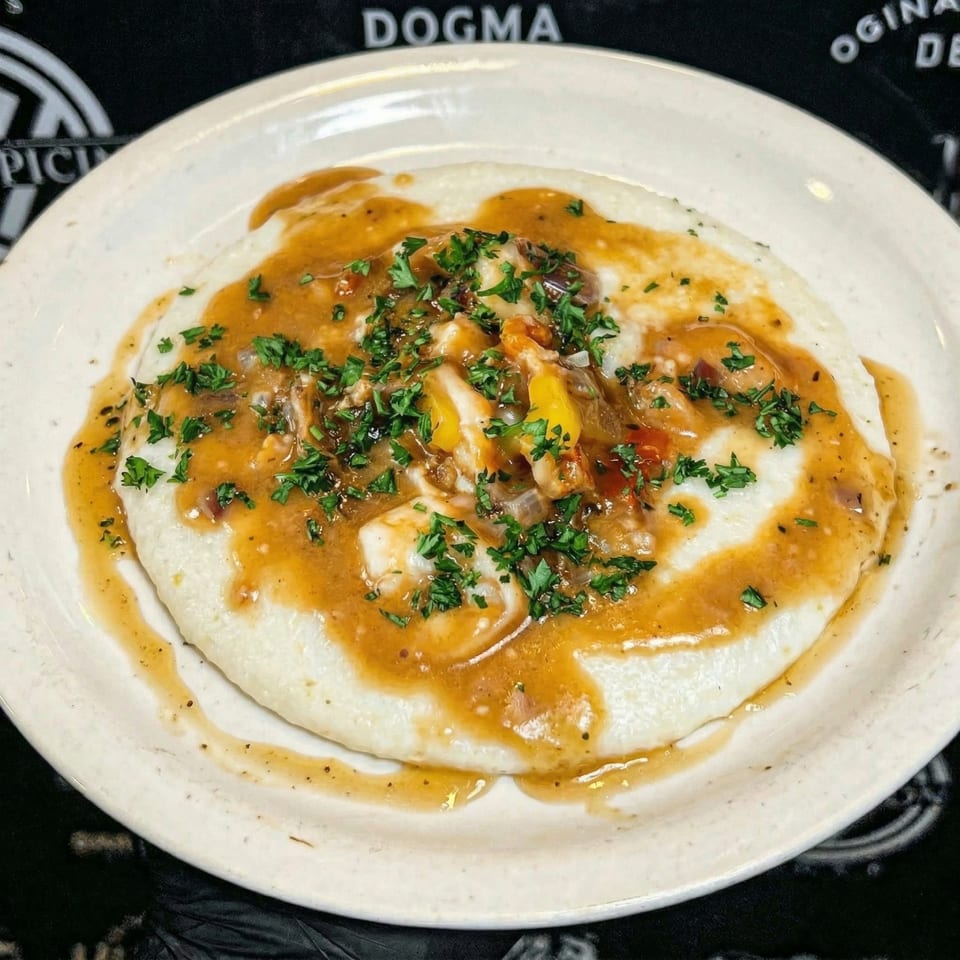 Creamy grits topped with shrimp, gravy, and fresh parsley on a white plate.