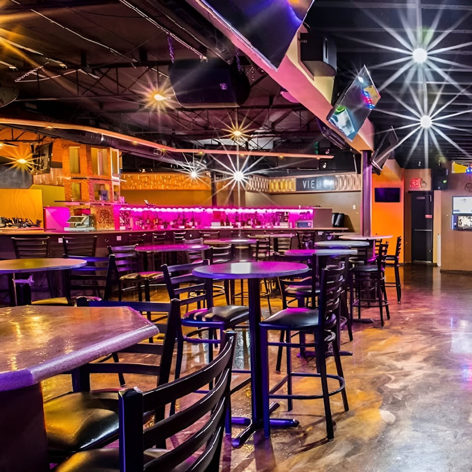 Interior of Views Bar & Grill with high-top tables, chairs, and a bar lit with pink neon lights.