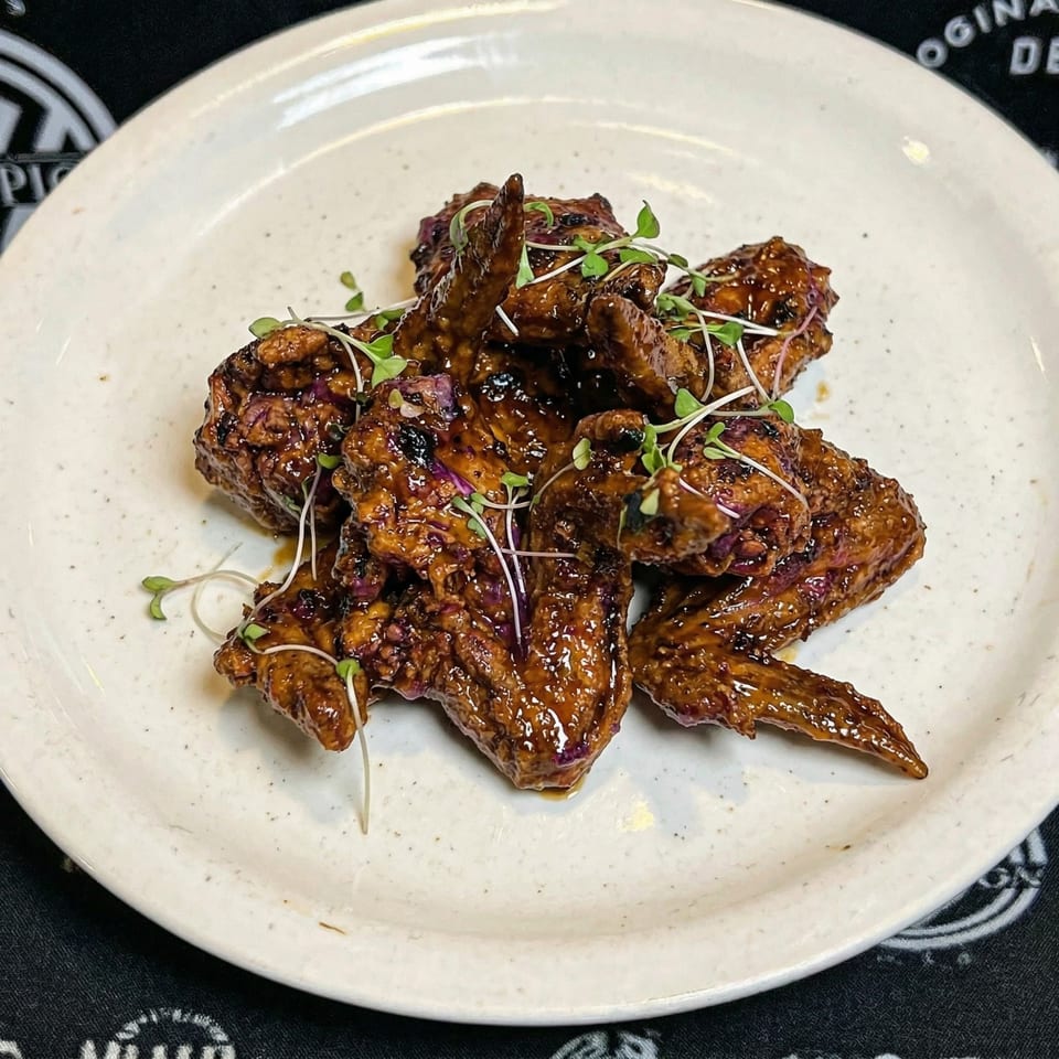 Glazed chicken wings with microgreens on a white plate, against a dark background.
