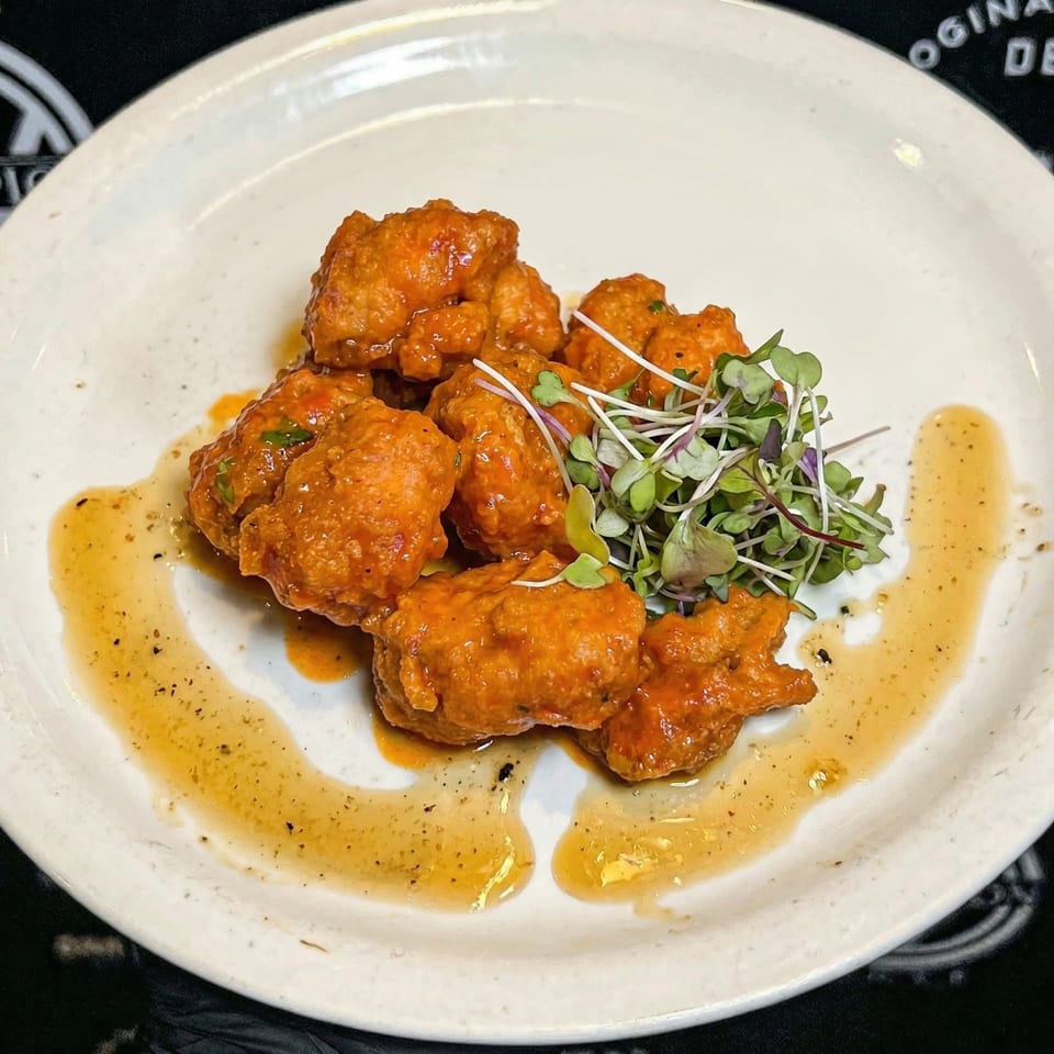 Crispy orange chicken bites with microgreens and a sweet chili drizzle on a white plate.
