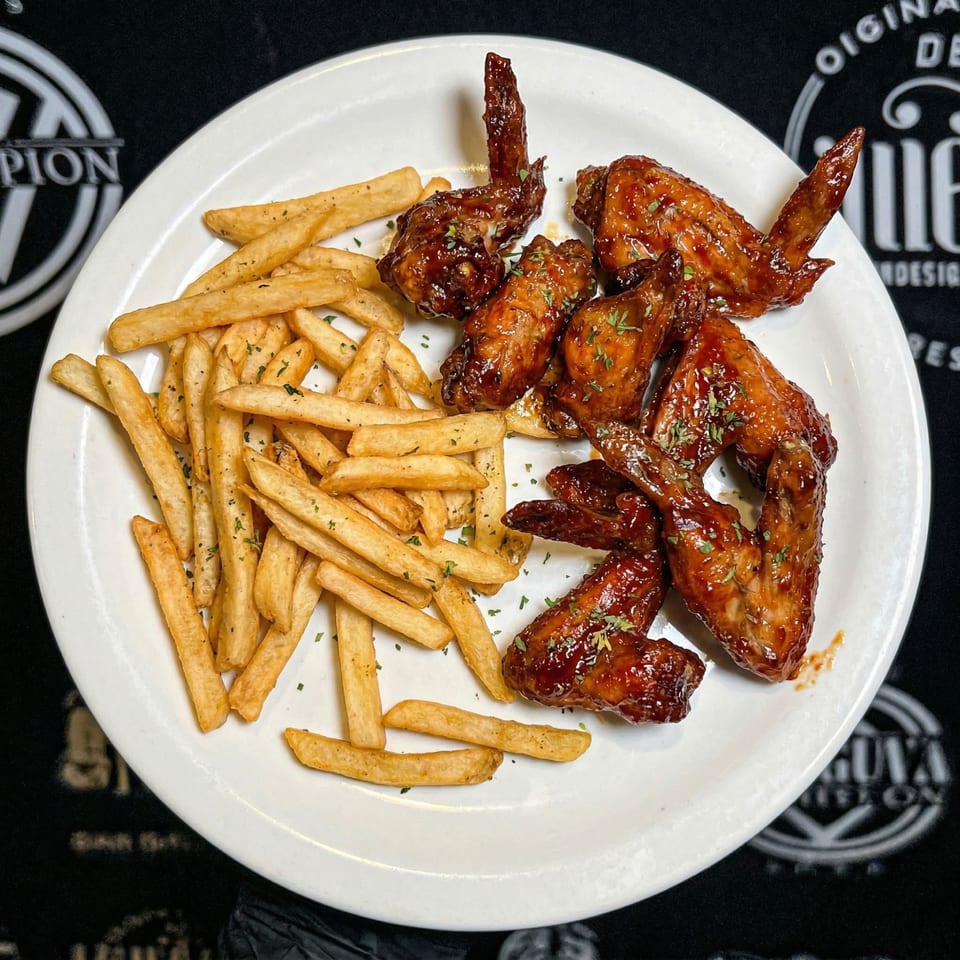 A white plate with crispy french fries and glazed chicken wings, garnished with herbs.