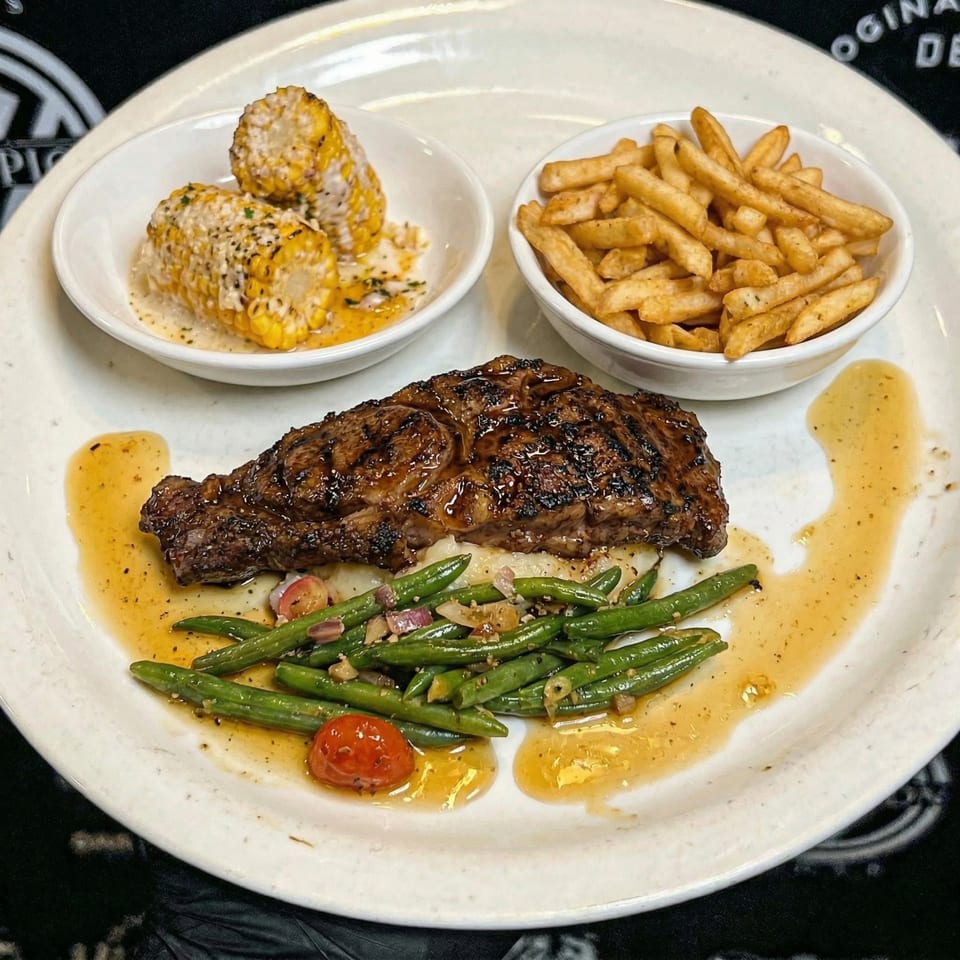 Grilled steak with green beans, cherry tomatoes, corn on the cob, and french fries on a white plate.