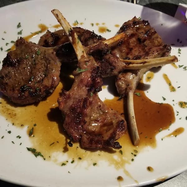 Grilled lamb chops with sauce and herbs on a white plate.