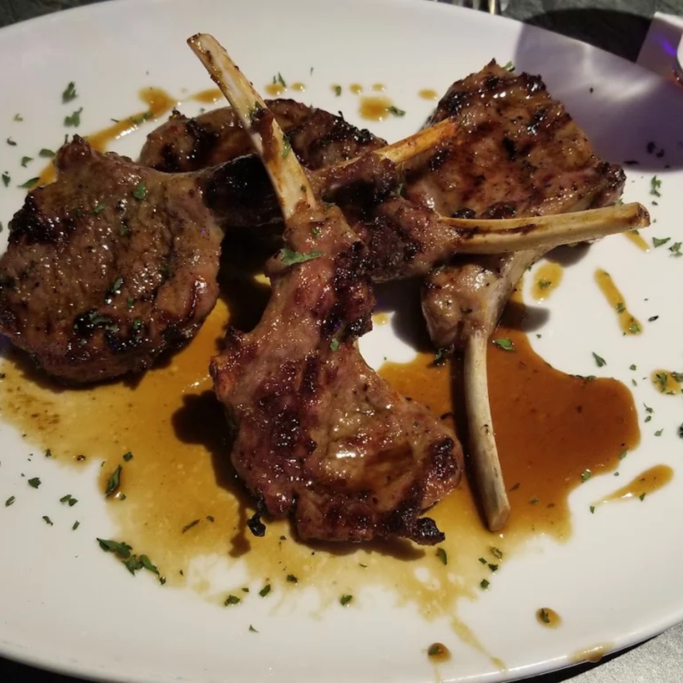 Grilled lamb chops with sauce and herbs on a white plate.