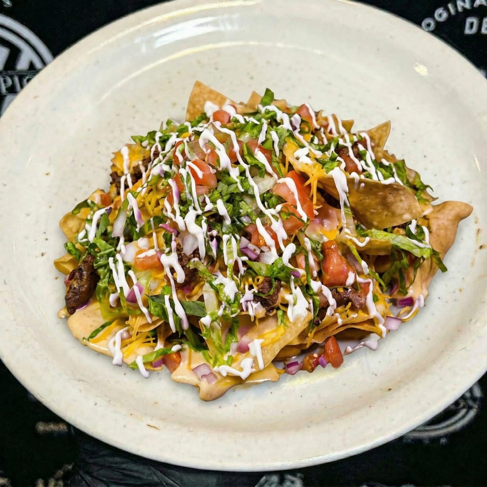 A plate of nachos topped with cheese, meat, lettuce, tomatoes, onions, and sour cream.